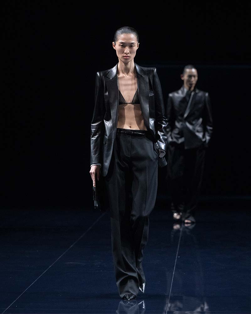 Zwart bikinitopje onder een zwart broekpak. Bikinitopje als integraal onderdeel van modelooks. Photo courtesy of Tom Ford