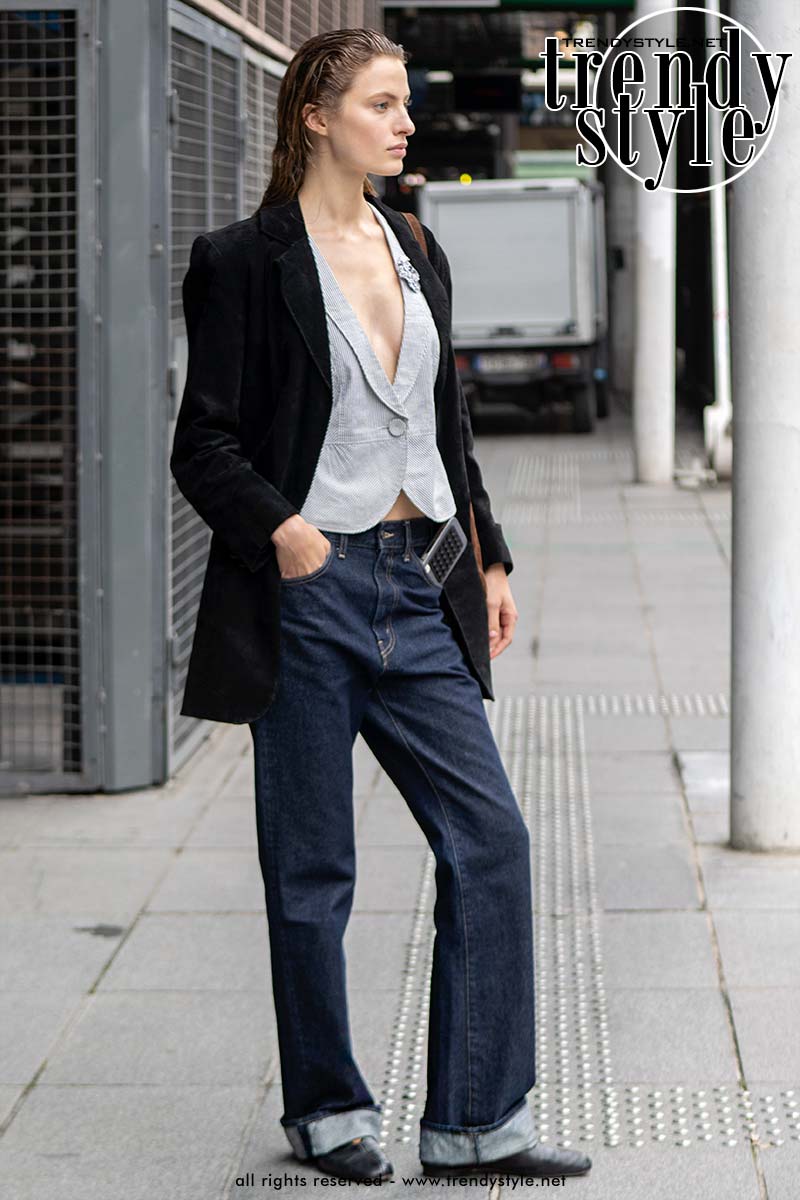 Model draagt een donkere jeans met omgeslagen pijpen, zwarte ballerina’s, een gilet en een donkere blazer tijdens Paris Fashion Week herfst winter 2026 2027. Foto Charlotte Mesman