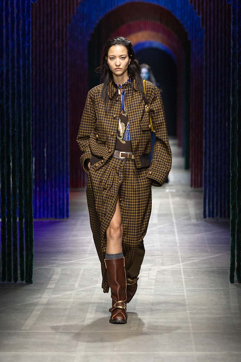 Model op de catwalk in een bruin setje met okergele windowpane-ruit (vensterruit), bestaande uit een kort jasje en een lange rok, gecombineerd met bruine laarzen. Photo courtesy of Etro