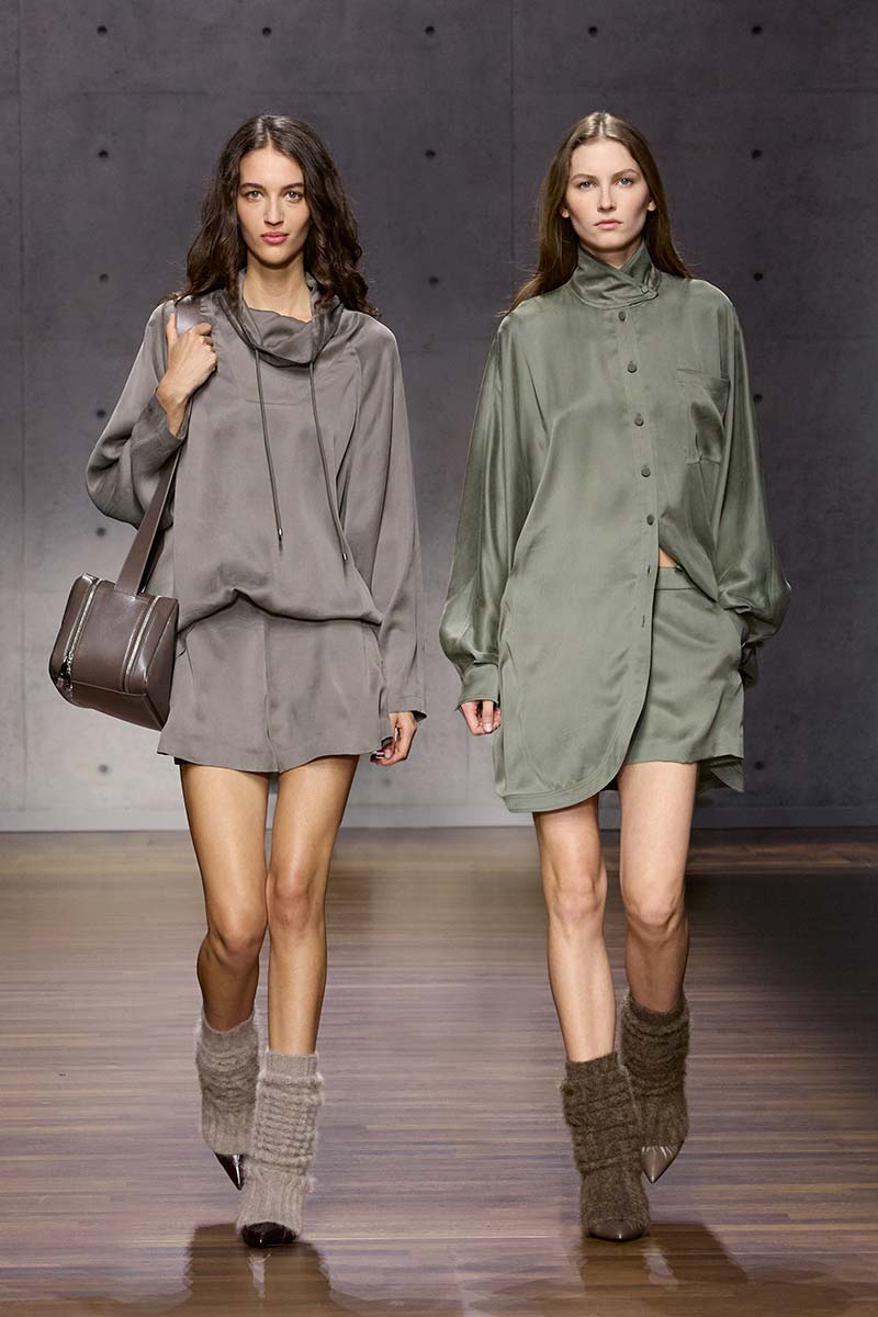 Twee modellen met lange, opgerolde beenwarmers, blote benen en pumps tijdens de Emporio Armani-catwalk voor herfst/winter 2026-2027. Photo courtesy of Emporio Armani