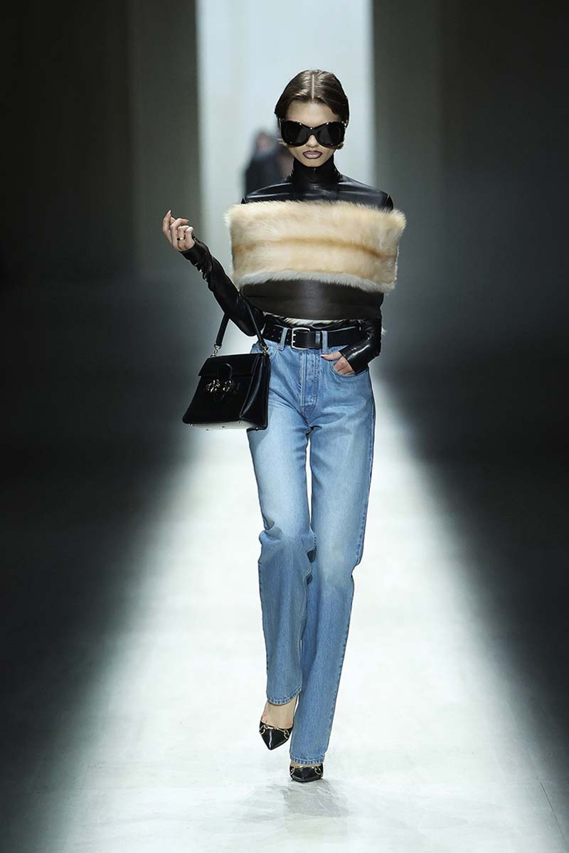 Model draagt een high-waisted straight jeans met zwarte coltop, beige bontstola en puntige zwarte pumps. Photo courtesy of Gucci