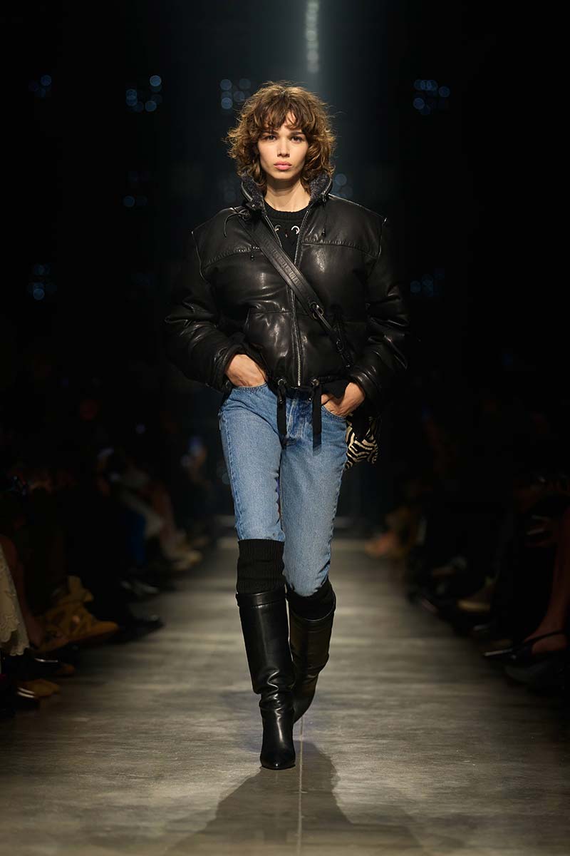 Model draagt een mid-wash straight jeans met zwart leren pufferjack en kniehoge laarzen met overknee kousen. Photo courtesy of Isabel Marant