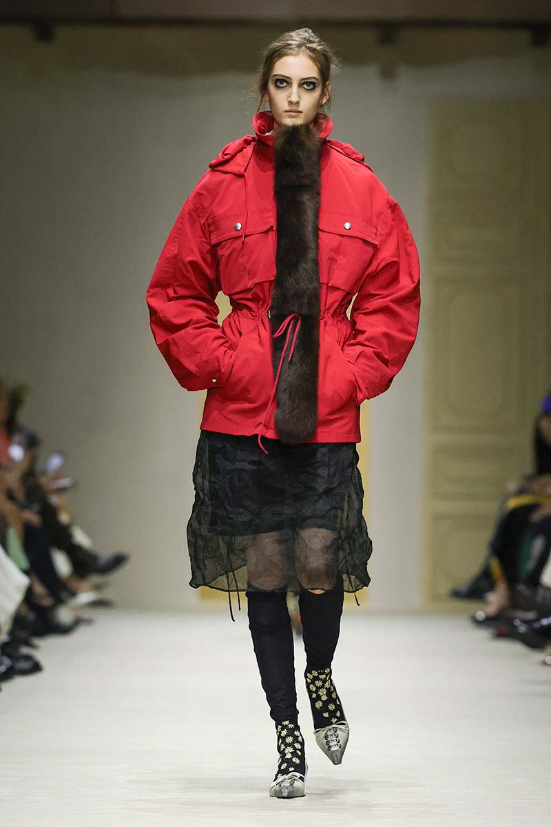 Prada combineert verfijnde pumps met korsetdetails en zwarte kousen met een sportief rood jack en 'dubbele' rok voor herfst/winter 2026/2027. Photo courtesy of Prada
