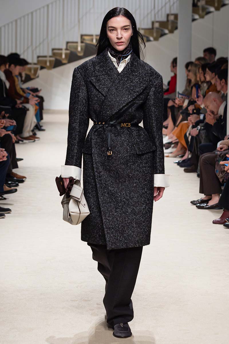 Donkere visgraatjas met brede schouders en leren ceintuur, gecombineerd met een wit overhemd, zijden sjaal en zwarte broek. Photo courtesy of Tod’s