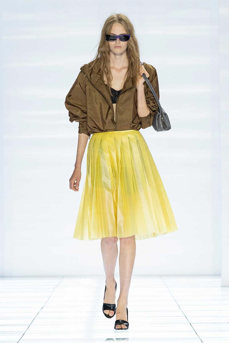 Een olijfgroen windjack in combinatie met een gele plooirok bij Prada. Photo courtesy of Prada